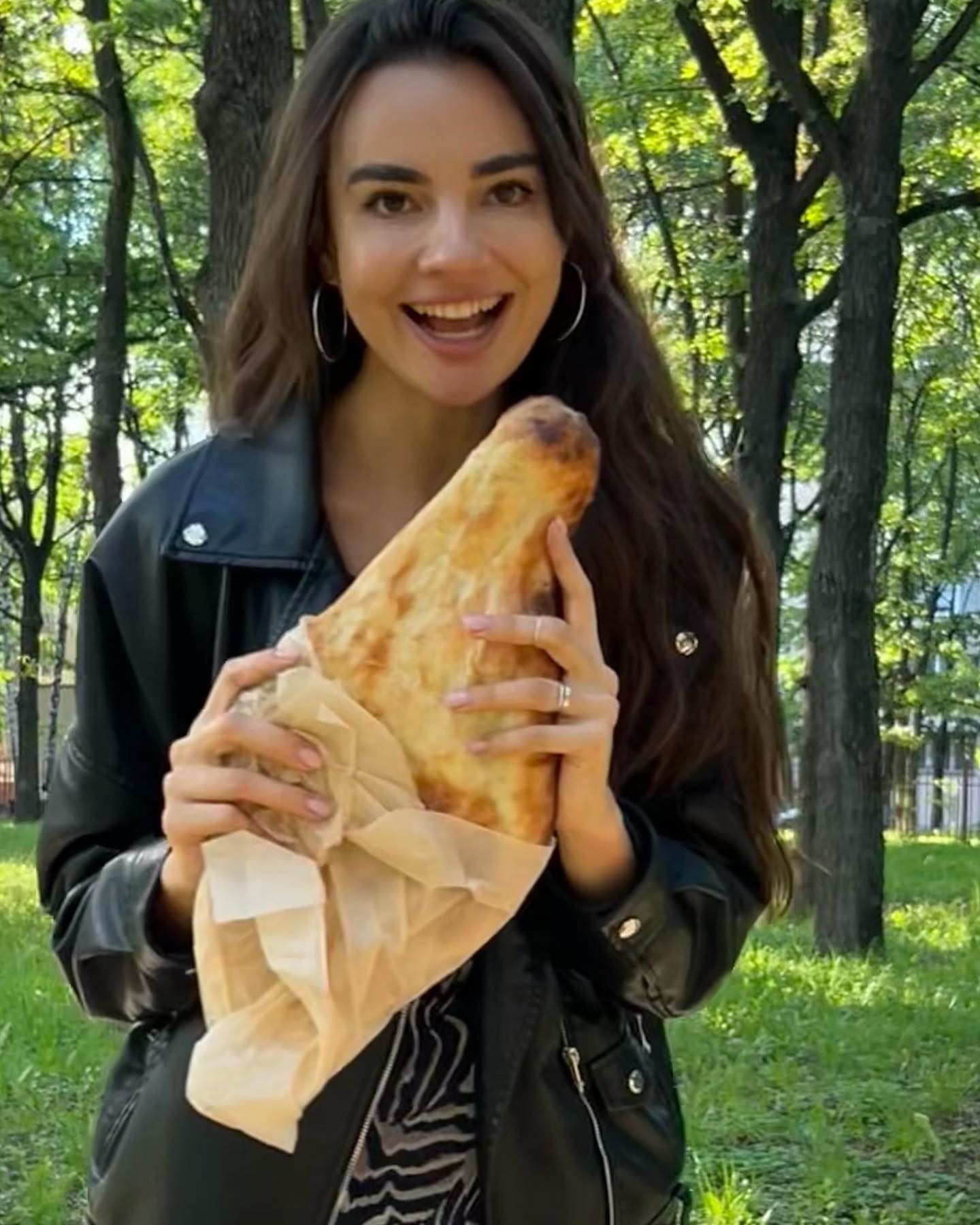 Сюзанна улыбается, держа в руках большое хачапури, на прогулке в парке